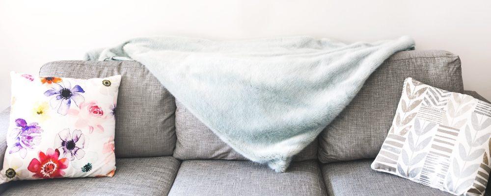 A grey sofa with cushions and a throw