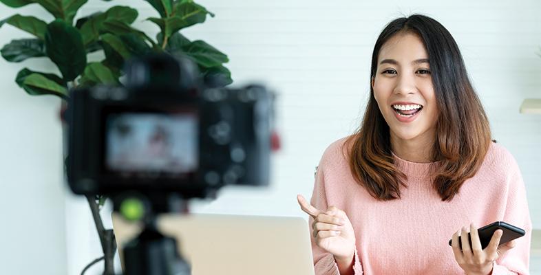 A women vlogger sat on a couch in front of a camera recording a film