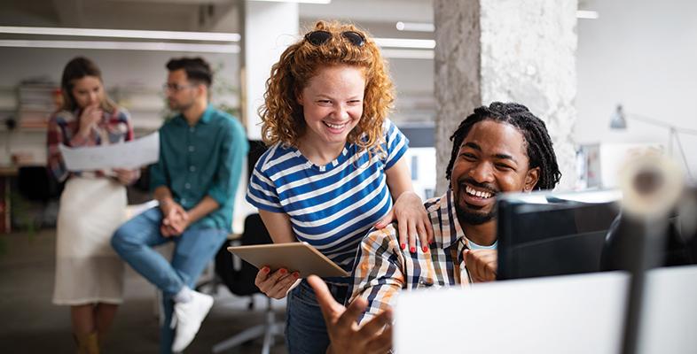 A male and female at a workstation looking at a laptop and smiling in a relaxed setting