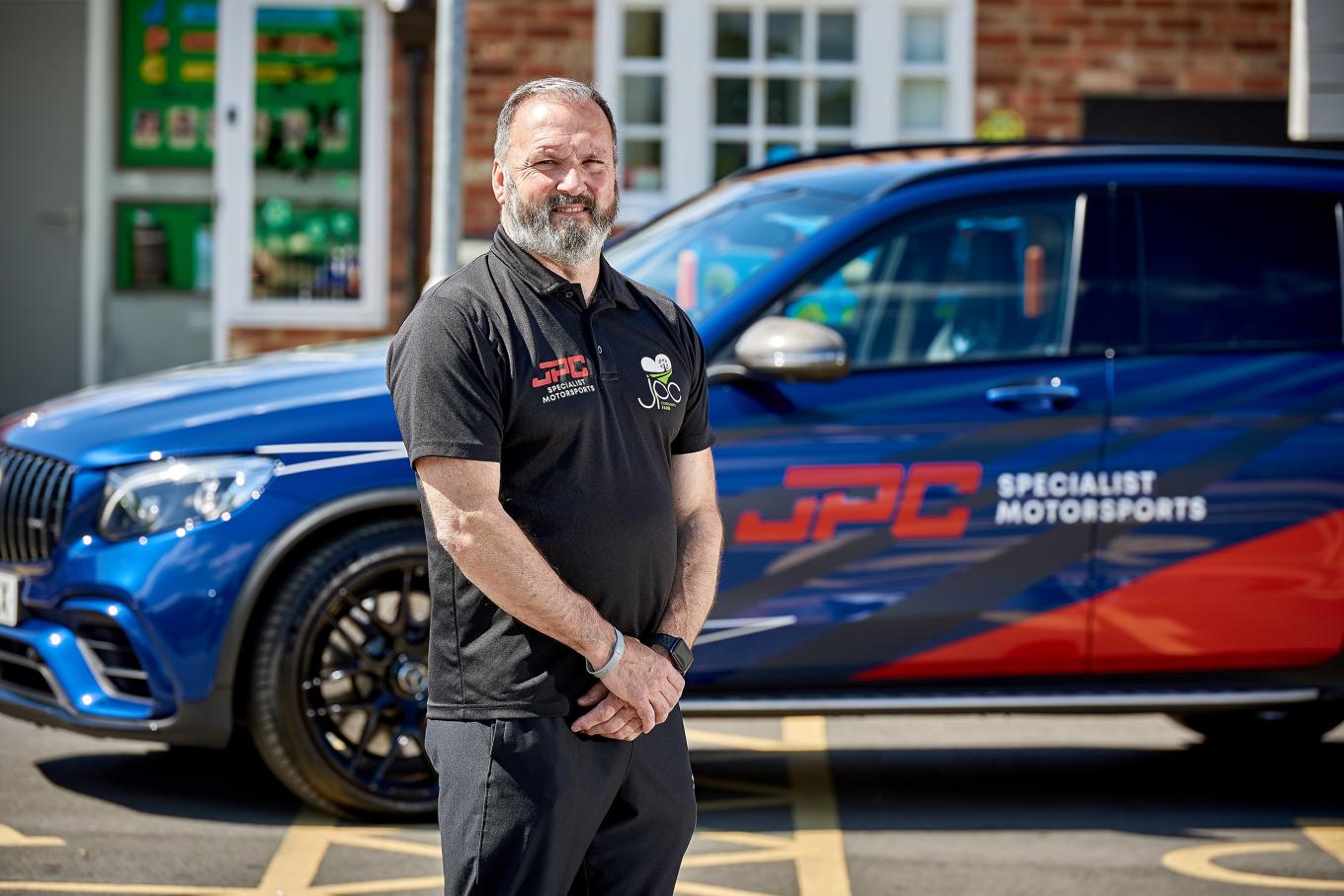 Business owner of JPC Community Farm standing in front of a branded sports car