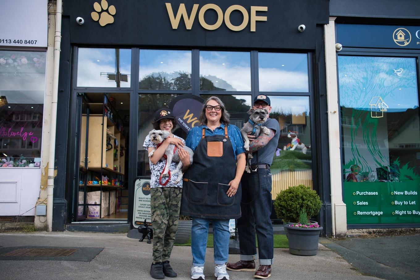 Business owner in front of her shop Woof surrounded by two people holding dogs