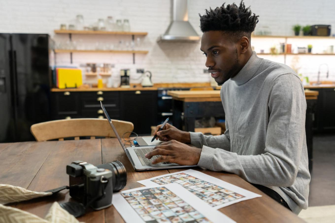 man at desk looking at laptop with camera and photos on it