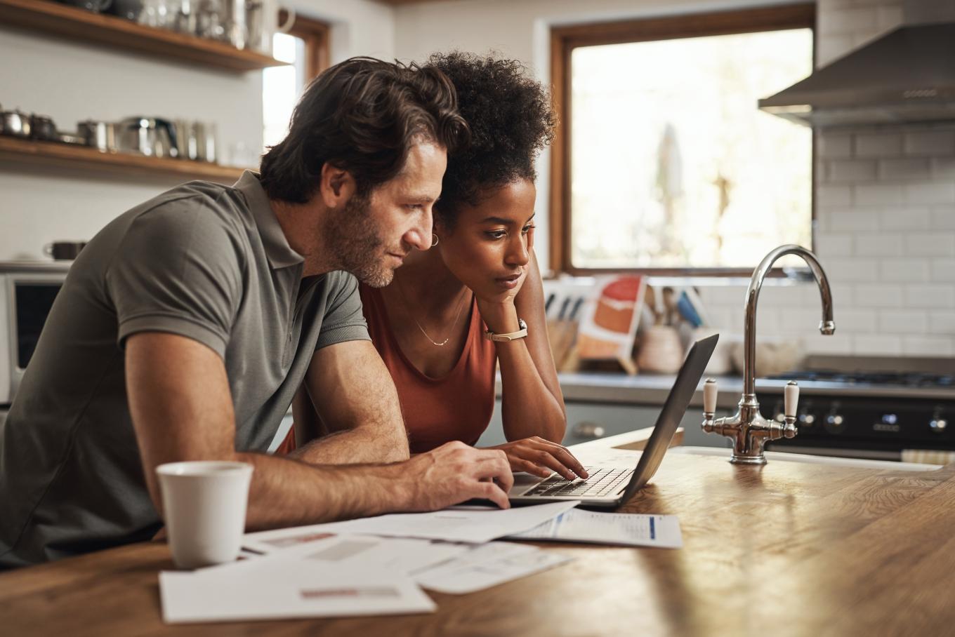 A male and female sat at a kitchen table looking at a laptop screen