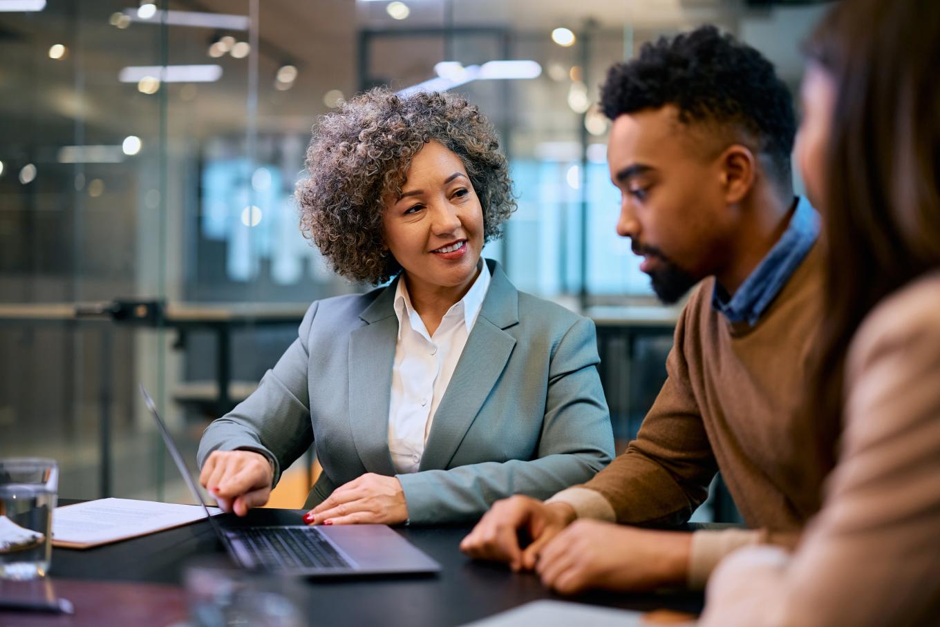Two females either side of a male at a desk in a modern office environment looking at a laptop screen