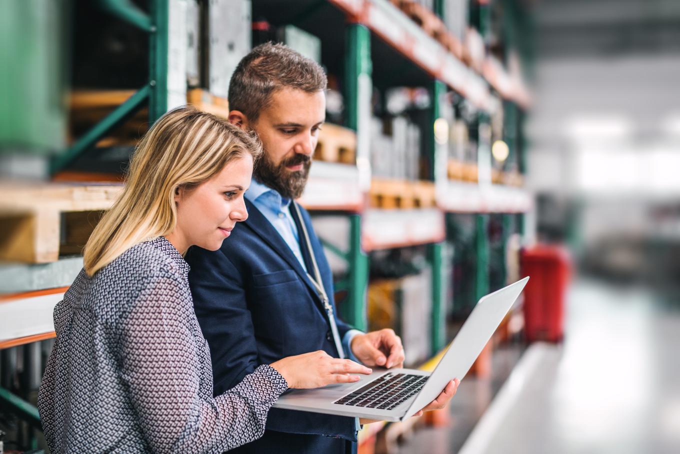 A male and female colleague in a warehouse environment looking at a laptop device