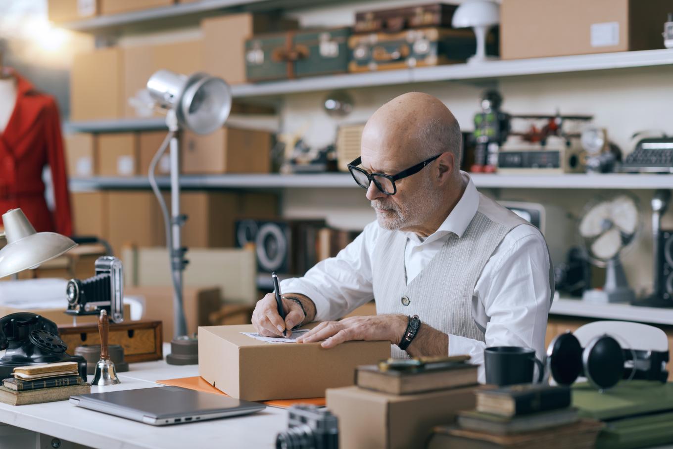 A tailor sat at a desk packaging, surrounded by equipment, fabric and a mannequin