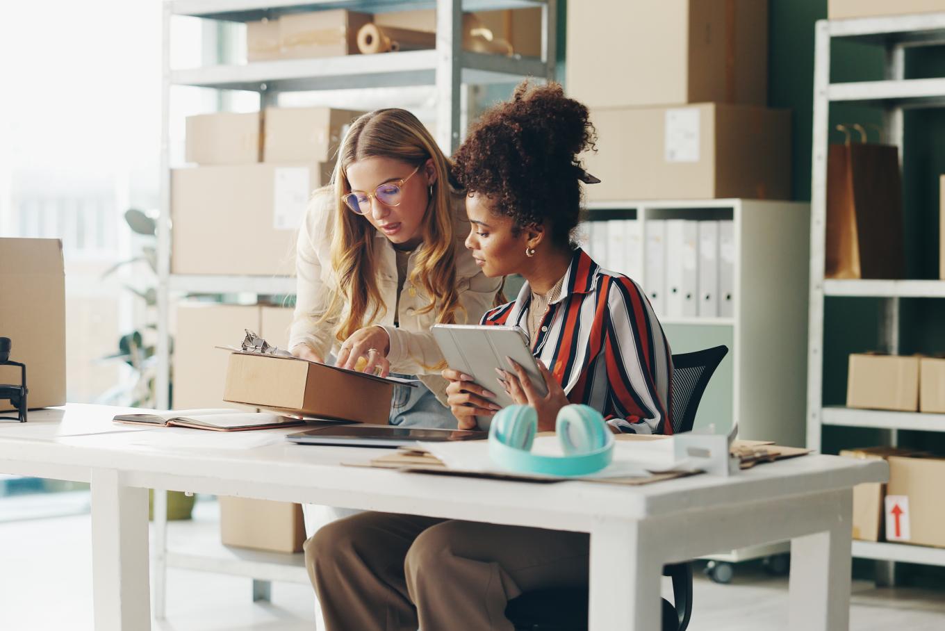 Two females set at a desk in a packing office preparing packages for postage