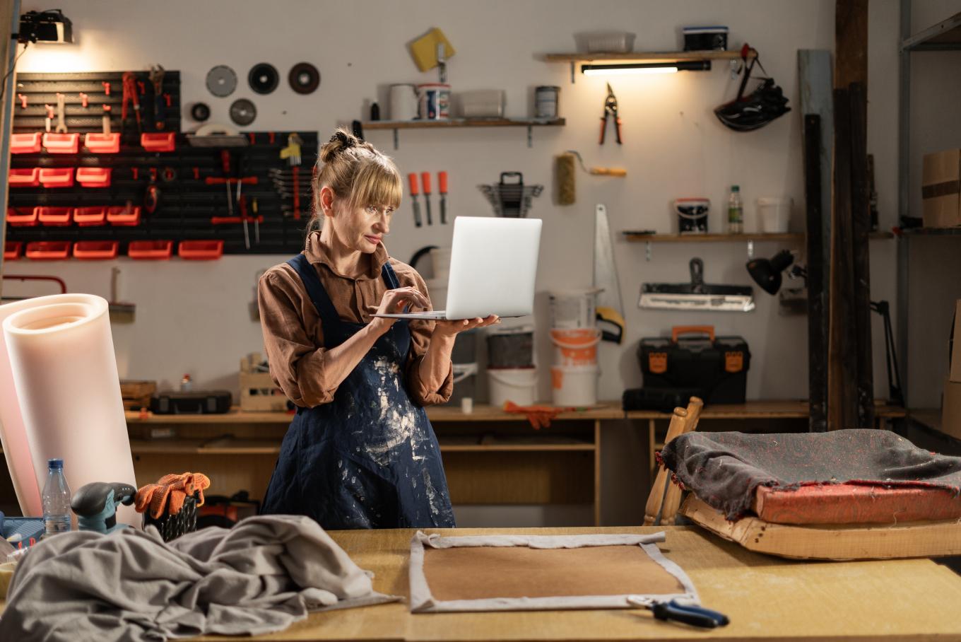 A female standing in a workshop at a bench holding a laptop in the air
