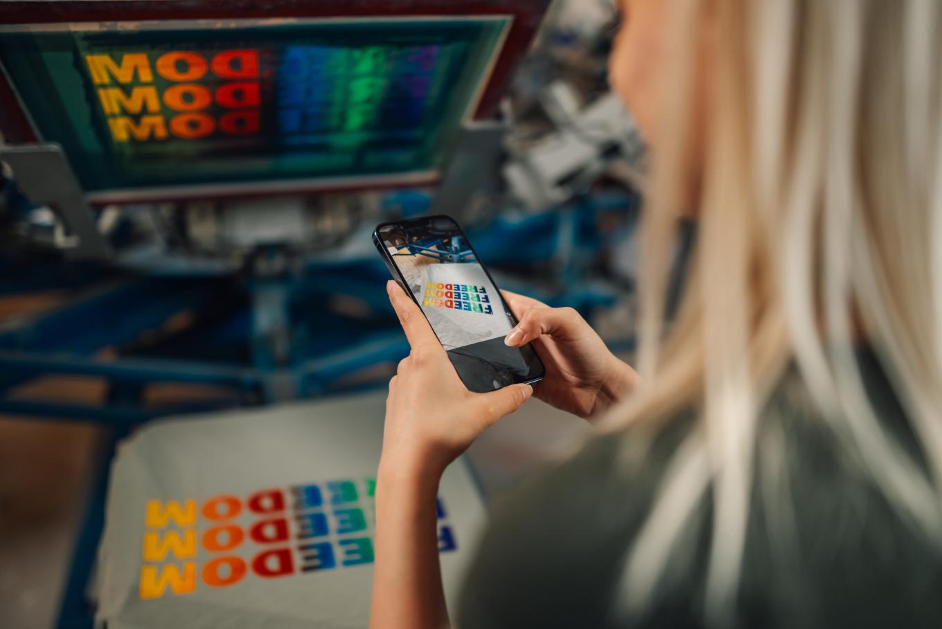 Image of a woman taking a photograph of some colourful wording that appears on a computer screen