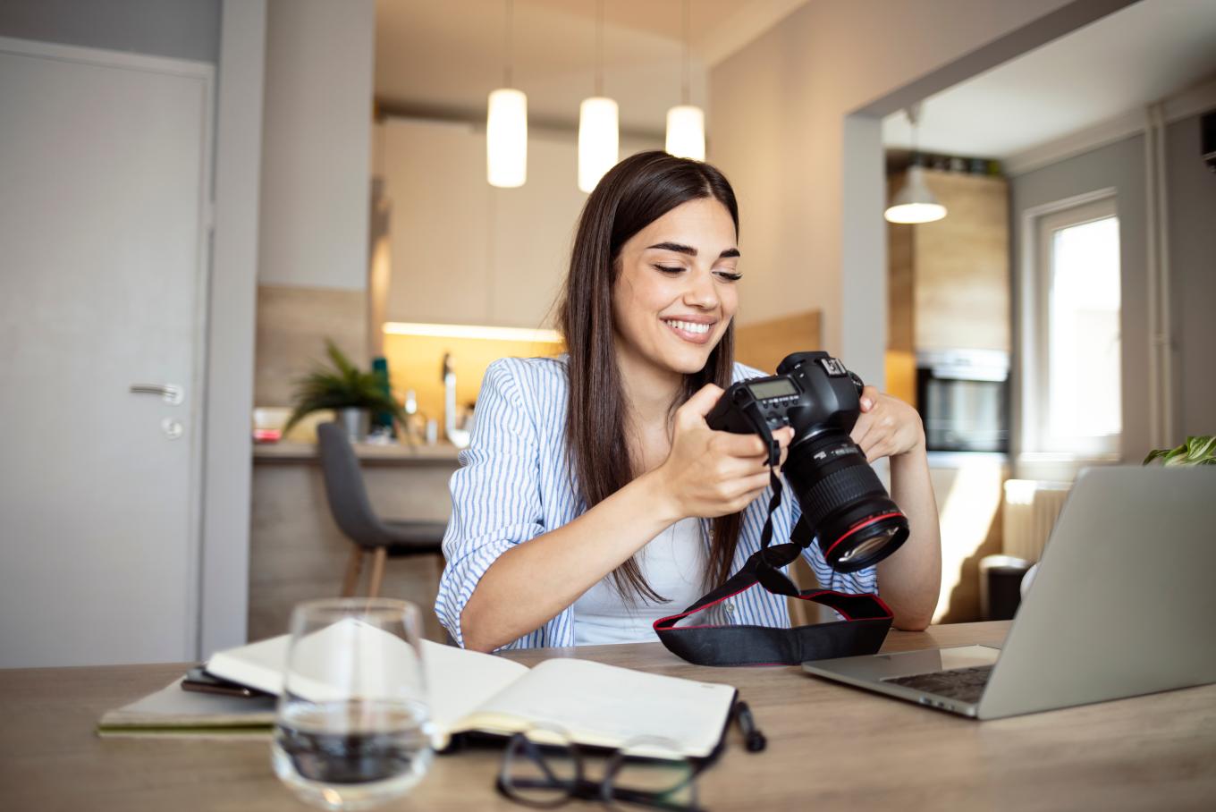 A young female photographer holding her camera sat at a desk looking at a laptop