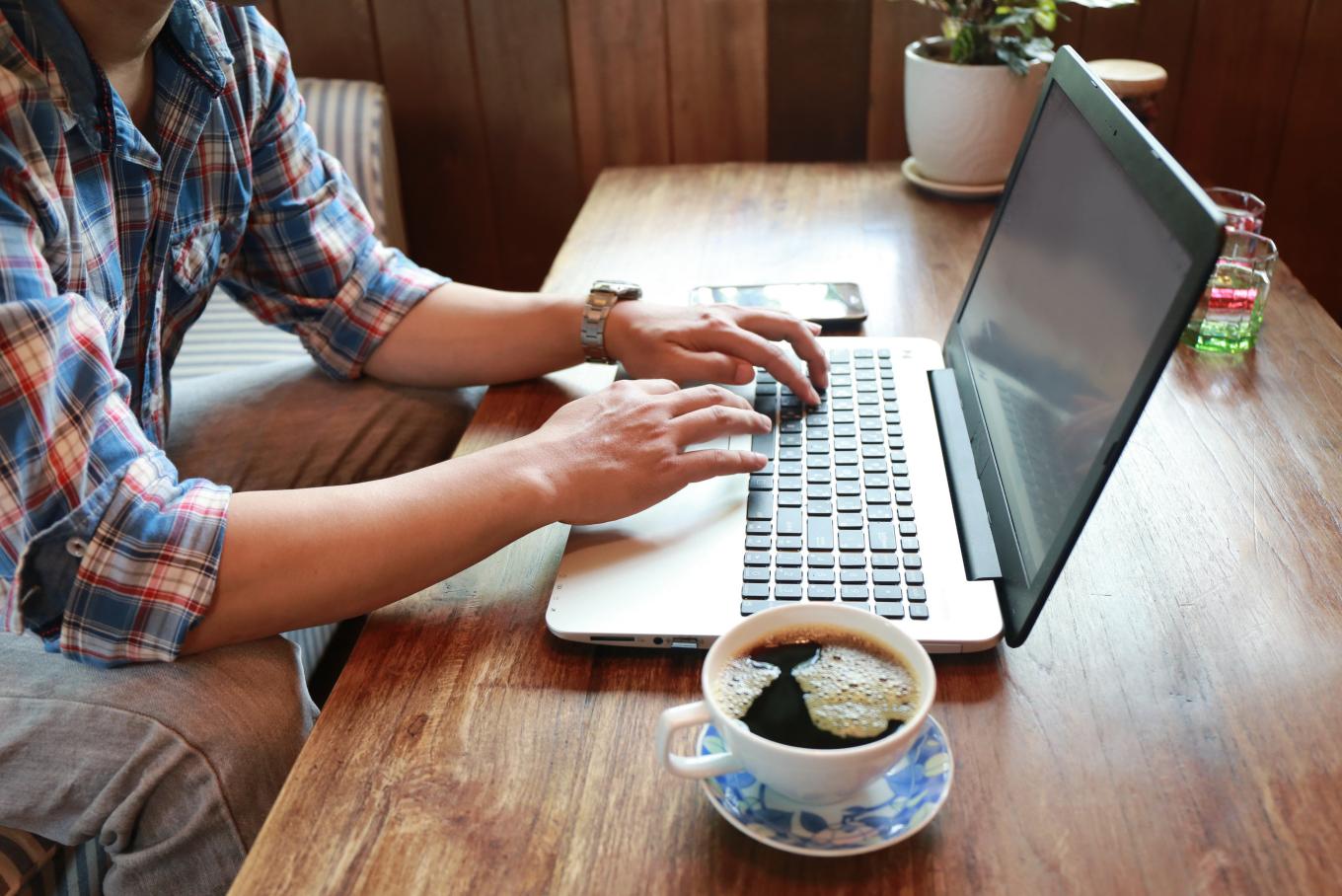 A person sat a desk typing away at a laptop with a cup of black coffee to the side of them