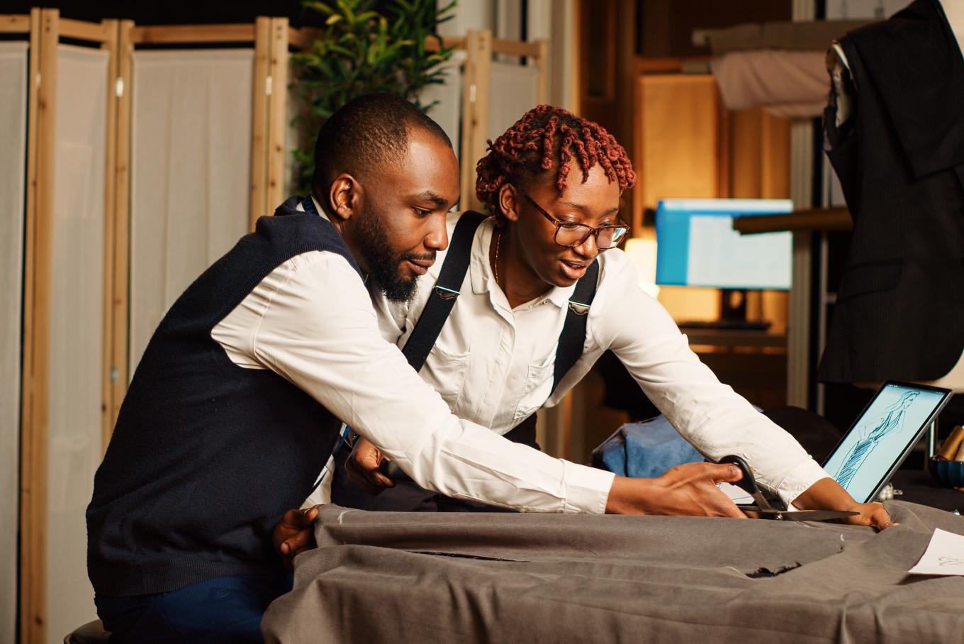 Two well tailored people stood next to each other looking at a laptop screen on a desk